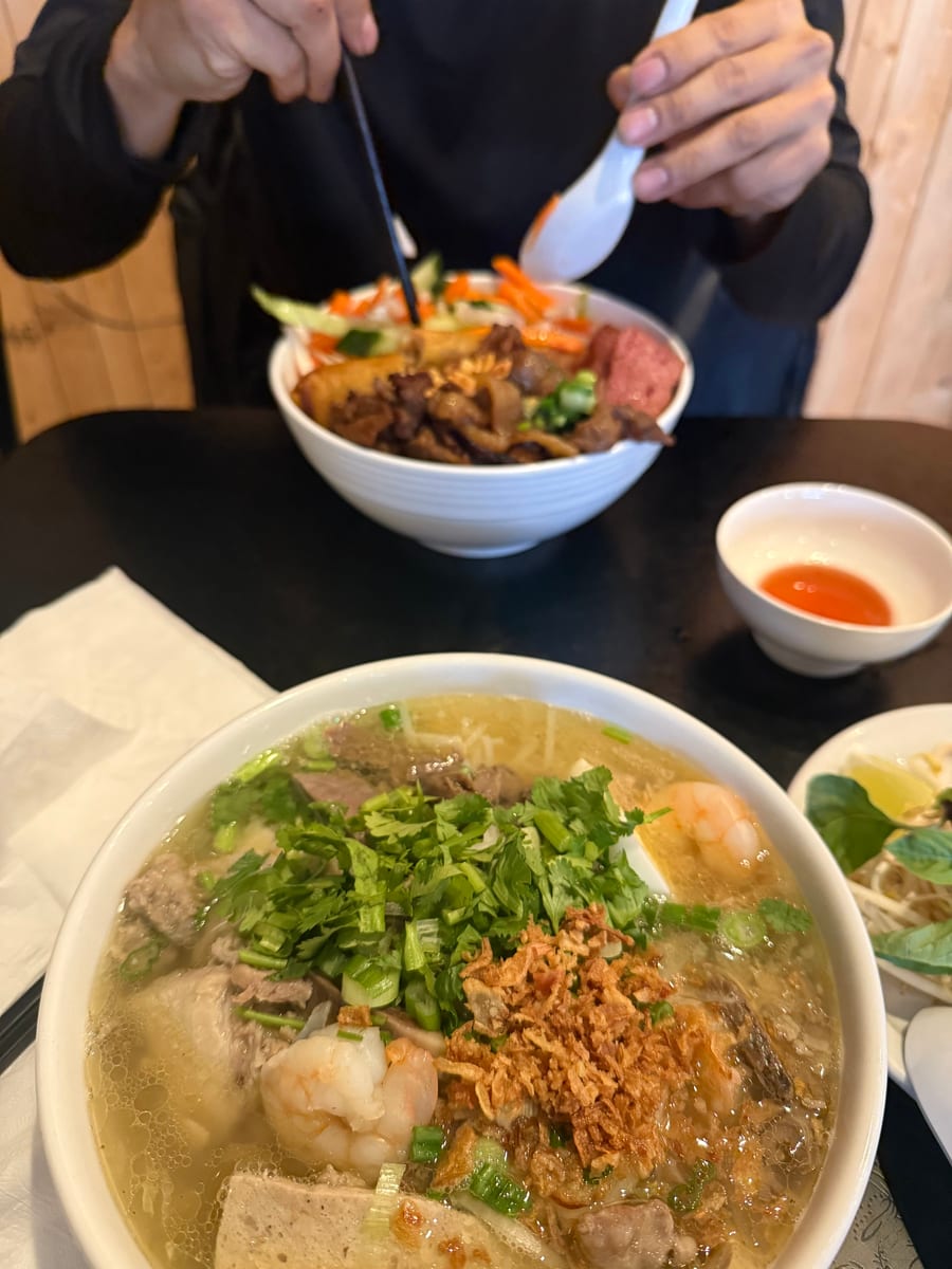 A bowl of pho with rare beef and a vermicelli bowl on a dark table
