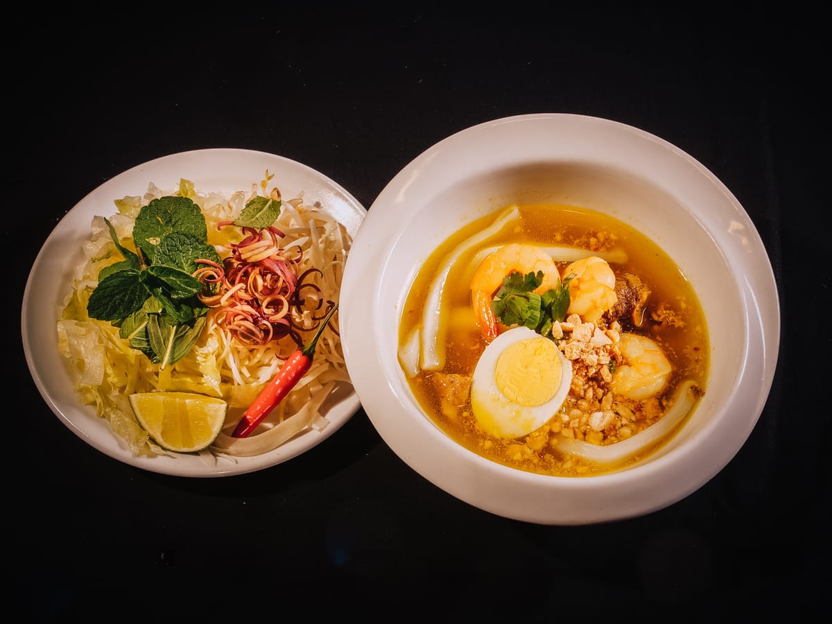 Two bowls of Mi Quang with shrimp, egg, peanuts and herbs